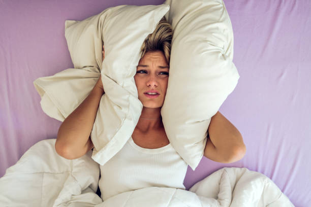 chica desesperada que sufre insomnio tratando de dormir. mujeres jóvenes angustiadas. una mujer tratando de dormir cubriéndose los oídos para evitar el ruido del vecino en casa durante el día. - hand to ear fotografías e imágenes de stock