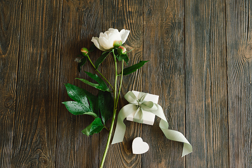 Bouquet of beautiful white peonies with gift boxes on wood background. Stylish floral greetings. Mothers day