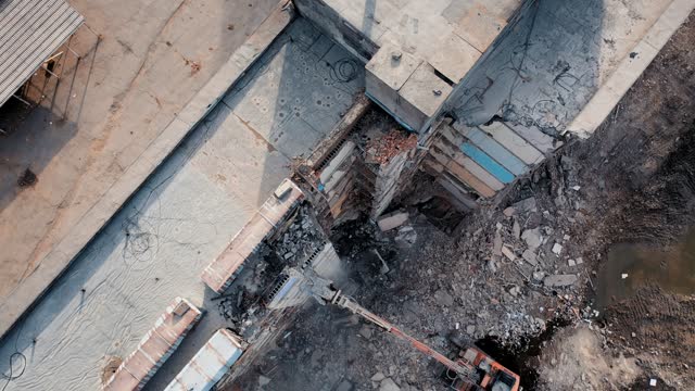 Tall building destroyed. Demolition machine tearing down roof of a wrecked building. Long machine claw pulling down the debris.