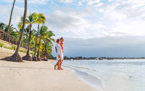istock Couple in love hugging on sandy exotic beach while having evening walk by Trou-aux-Biches seashore on Mauritius island enjoying sunset. People relationship and tropic honeymoon vacations concept image 1496925462