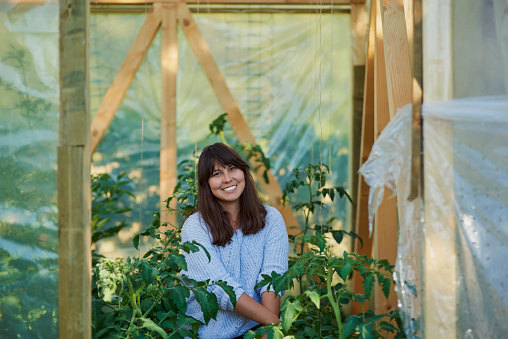 Woman, greenhouse and smile in portrait with plants for agriculture, quality assurance and growth. Female farmer, botanist and leaves at agro nursery for health, development and sustainable gardening