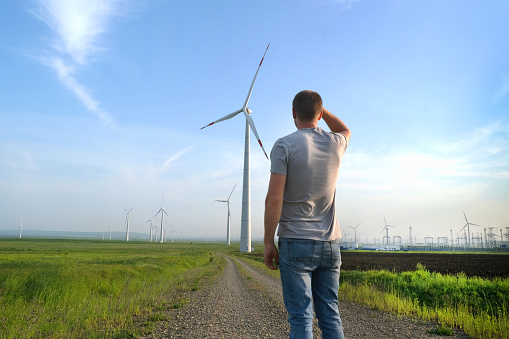 The man stands with his back and looks at the wind turbine. Wind Energy Park.