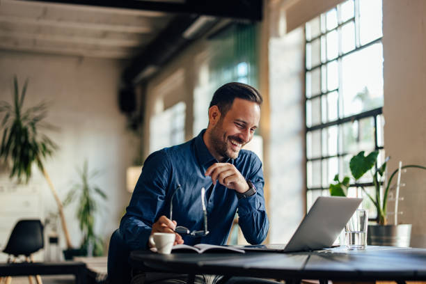 istock Smiling businessman using a laptop, working at the office, holding his glasses. 1496935366