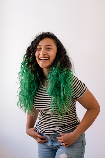 Portrait of a young woman with dip dyed green hair standing looking at the camera laughing while at a studio in the North East of England.