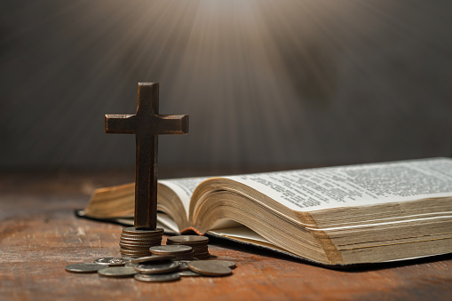 Stack of coin money, holy bible book and old wallet on wooden table. Copy space, a closeup. Christian biblical concept of tithing, giving, and religious offering.