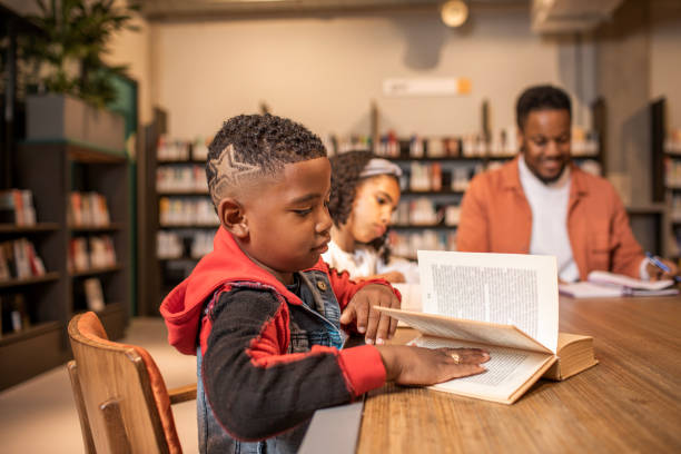 un maestro negro adulto joven con un lector infantil diverso en una biblioteca - e reader cheerful indoors lifestyles fotografías e imágenes de stock