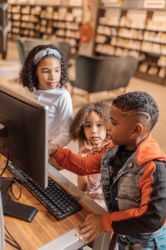 Three young black readers using a computer in a library