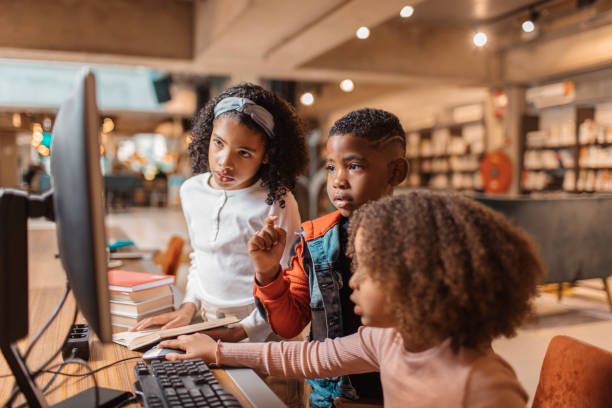 Three young black readers using a computer in a library stock photo