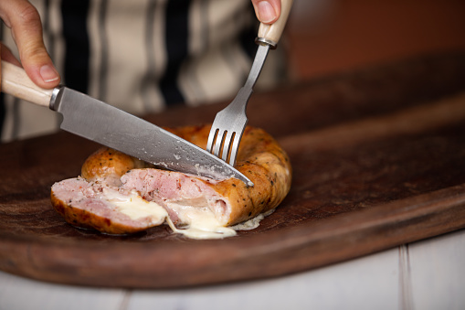 Unrecognizable person cutting grilled chorizo ​​sausages with fork and knife - Buenos Aires - Argentina