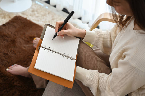 istock Top view and close up with Asian female writing something on the diary book while sitting on the armchair at home. 1496942349