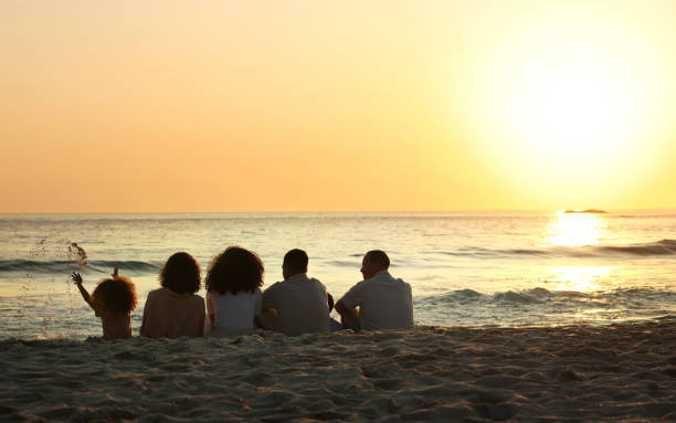 istock Big family, sunset view and back at beach, having fun and bonding on vacation outdoors mockup. Care, love and children, grandmother and grandfather with parents sitting and enjoying holiday time. 1496945495