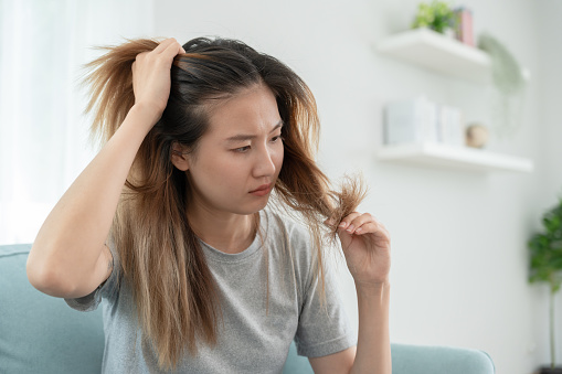 Asian woman very sad and upset looking at damaged hair, hair loss, hair thinning problem, vitamin deficiency, baldness, postpartum, biotin, zinc, menstrual or endocrine disorders, hormonal imbalance