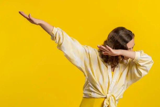 Photo of Cheerful woman having fun dancing, moving to rhythm, dabbing raising hands, making dub dance gesture