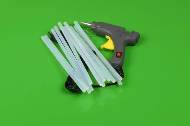 Electric hot glue gun with gluestick isolated on green background. High resolution photo. Full depth of field.