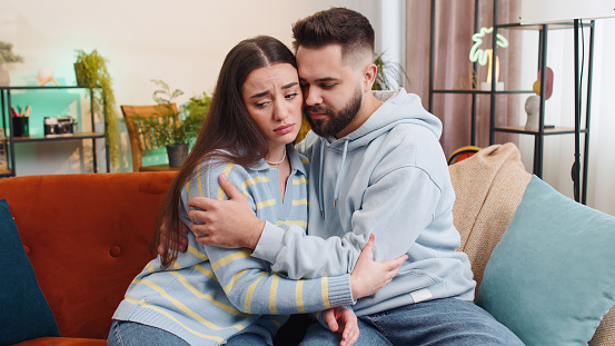 Compassion. Man supporting depressed offended woman of bad pregnancy test results. Sadness stress suffers from breaking up quarrel in work. Husband and wife family marriage couple together on sofa