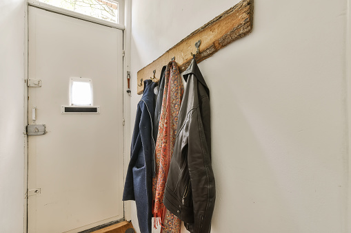 a coat rack on the wall next to a white door with clothes hanging on it and a black leather jacket hanger