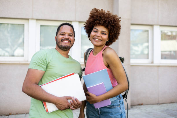 istock Two dark-skinned young millennials pose with textbooks and backpacks outside the university. The chubby Dominican man and the woman with the afro hair look at the camera happily. Multiethnic concept. 1496951472