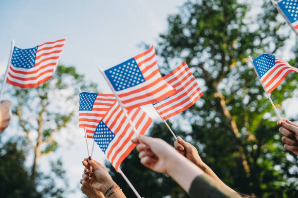 A group of people is waving small American flags at sunset A group of people is waving small American flags at sunset. Concept for various topics like Happy Veterans Day, Labour Day, Independence Day. 21 24 months stock pictures, royalty-free photos & images