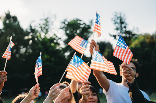 A group of people is waving small American flags at sunset. Concept for various topics like Happy Veterans Day, Labour Day, Independence Day.