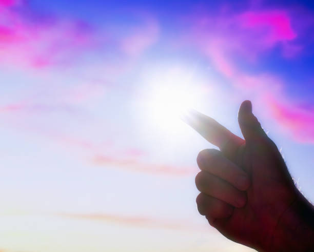 istock Man's back-lit hand points to the sun in a painterly pink and blue sky 1496951949