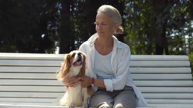 Senior woman sitting on bench with cavalier spaniel in park