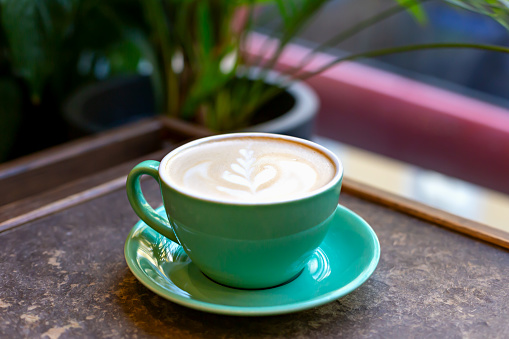 Fresh delicious aromatic coffee latte with pattern in green ceramic cup on table close-up. Selective focus