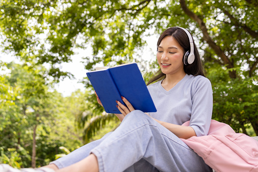 Asian woman reading a book and listen music during the day in the public park