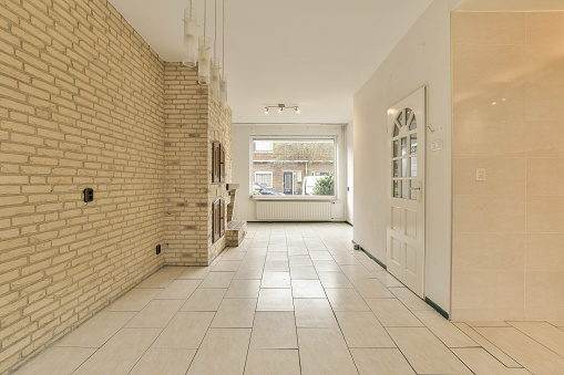 a long hallway with white tile on the floor and beige brick wall behind it, there is an open door that leads to another