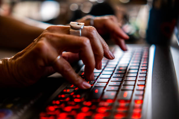 An anonymous programmer types code on the keyboard of a laptop computer backlit in red stock photo