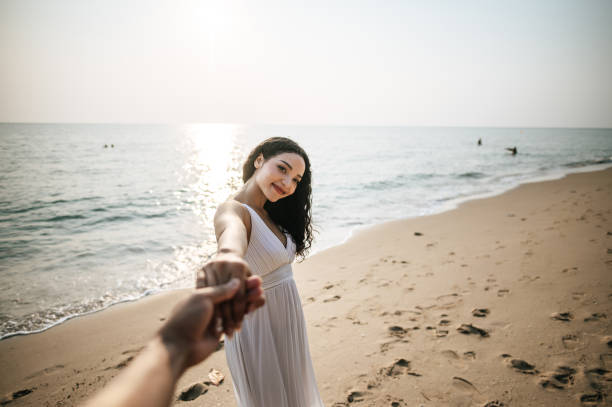 hermosa mujer de la mano con su novio mientras camina por la playa - honeymoon beach couple heterosexual couple fotografías e imágenes de stock