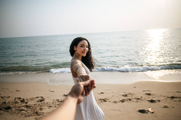 hermosa mujer de la mano con su novio mientras camina por la playa - honeymoon beach couple heterosexual couple fotografías e imágenes de stock