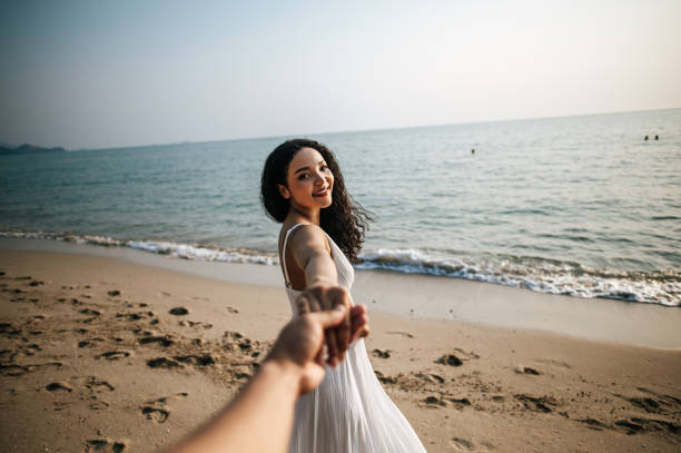 hermosa mujer de la mano con su novio mientras camina por la playa - honeymoon beach couple heterosexual couple fotografías e imágenes de stock