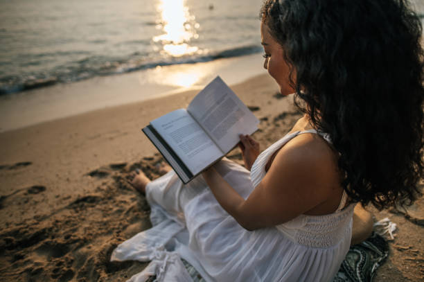 istock Young beautiful woman reading book during tropical beach vacation 1496961542