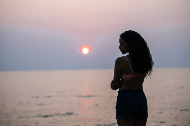 istock Lonely young woman standing alone on sandy beach by seaside in evening 1496961585