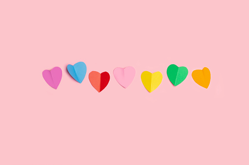 Colored paper hearts on a pink background with copy space