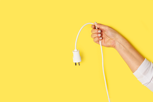 Woman hand holding a cord with plug on a yellow background with copy space