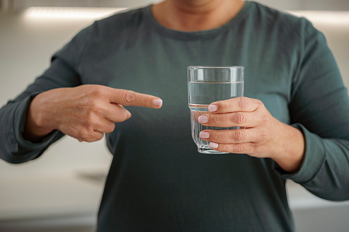 Front view of unrecognizable woman holding and pointing a drinking glass filled with water