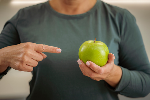 Front view of unrecognizable woman holding and pointing a green apple