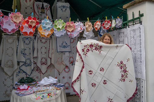 Budapest, Hungary - November 30th, 2022: A woman selling traditional hungarian table linens with lace and embroidery, showing her merchandise.