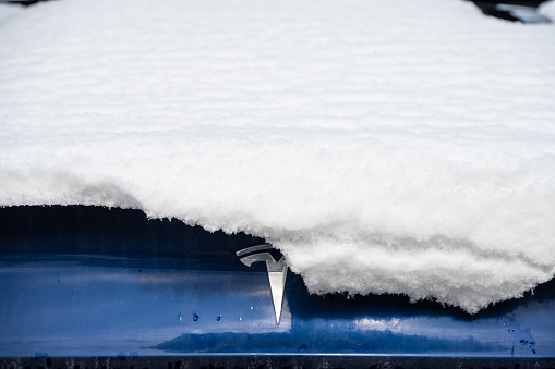 Gothenburg, Sweden - March 26 2023: Tesla logo on a blue car partially hidden by snow.