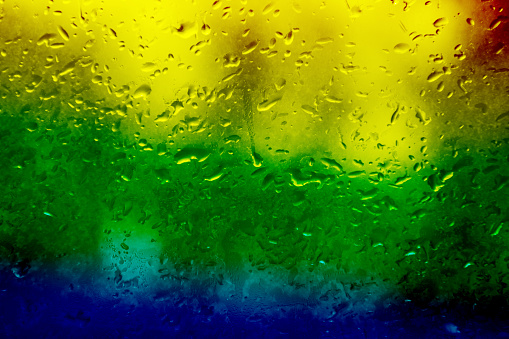 Glass with rain drops in rainbow colors. Raindrops on window closeup. Beautiful rainbow background
