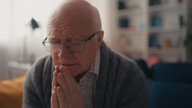 Senior man in glasses praying alone at home, religious beliefs, Catholicism