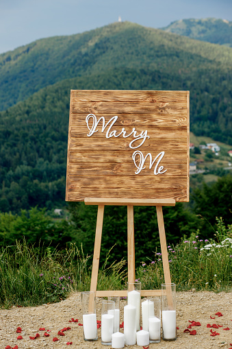 A romantic location in the mountains for a proposal of the hand and the heart Wooden easel with the inscription marry me. Mountain landscape.