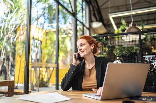 Happy young businesswoman talking on mobile phone and looking away at office