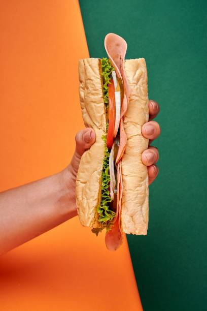 istock someone holding up their sandwich on the same hand with an orange background 1496986031