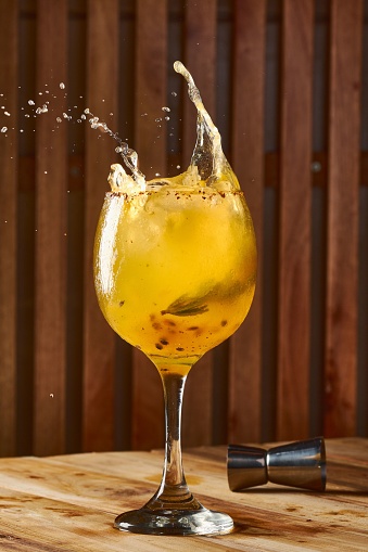 A large stemmed glass filled to the brim with a golden-hued liquid, droplets of water cascading down the sides as it splashes into the glass