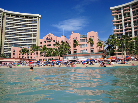 Honolulu, Oahu, Hawaii - February 17, 2011: Tourists enjoying the sun on Waikiki Beach outside the Royal Hawaiian Hotel, Honolulu, Hawaii. The distinctive coral pink hotel was built in 1927 and renovated in 2009. The modern Royal Beach Tower - pink balconies on the hotel's left - is part of the hotel, added in 1969.