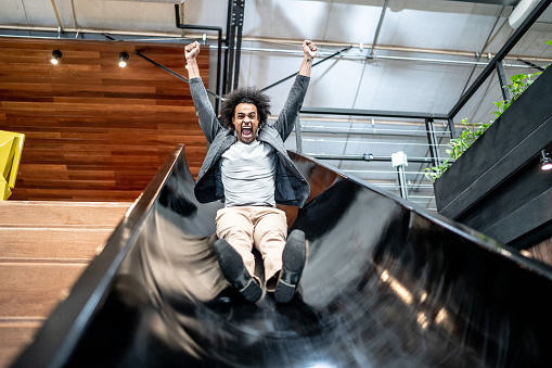 Young business man sliding down slide at coworking/office