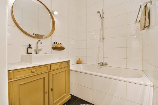 a bathroom with yellow cabinets and white tiles on the walls, along with a large round mirror in the corner