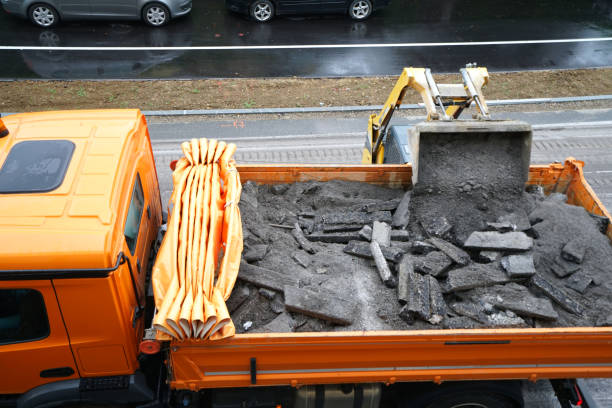 A small bulldozer loads the removed asphalt and road curbs into the dump tuck on road construction site. High angle view.